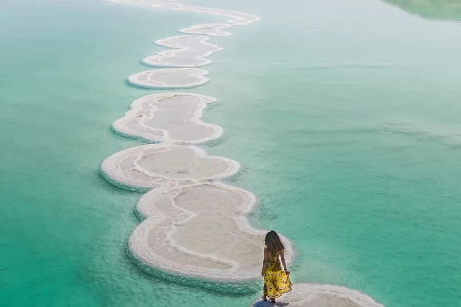 A person walking along salt formations in the turquoise water of the Dead Sea